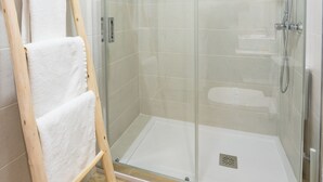 A glass-enclosed shower stall with a handheld showerhead and a handheld shower brush.