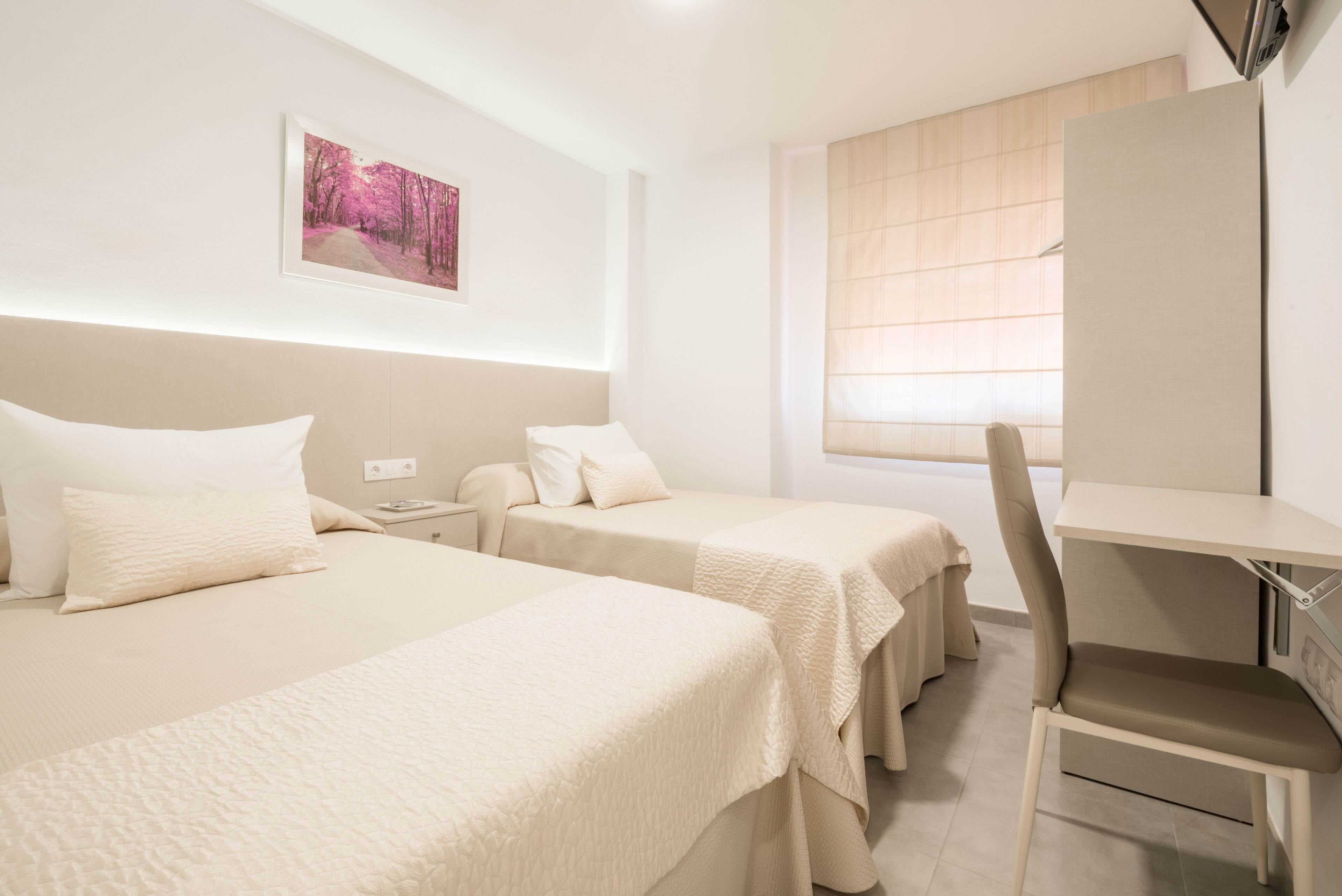 A hotel room with two beds, a desk, a chair, a window with blinds, and a framed picture on the wall.