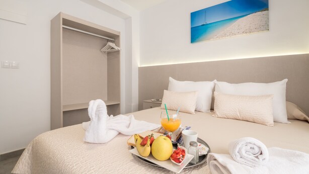 Habitación de hotel con una cama, una bandeja con frutas y una bebida, una toalla y un cuadro de una playa en la pared.