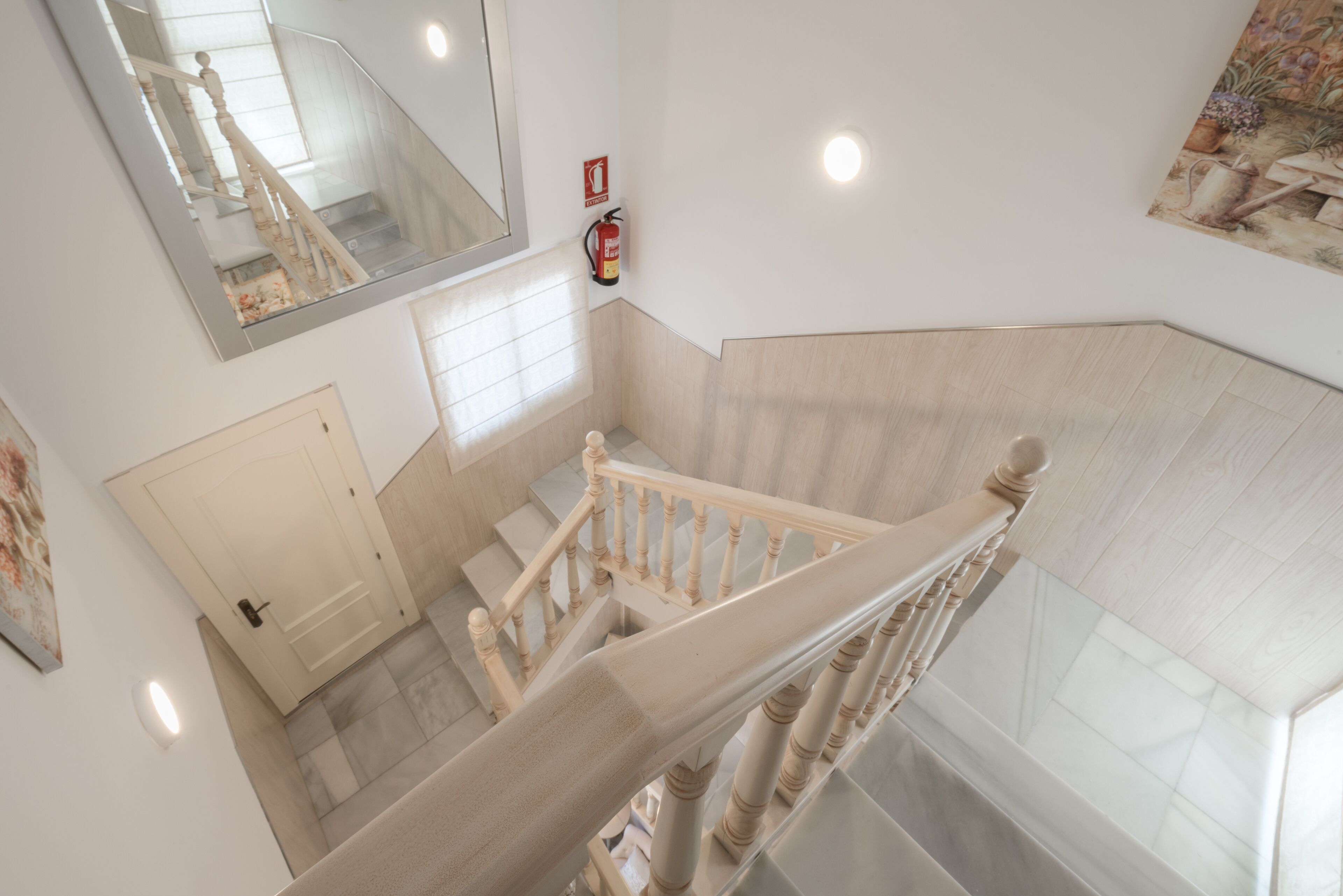 A modern interior with a wooden staircase, a fire extinguisher, a door, and a large mirror.