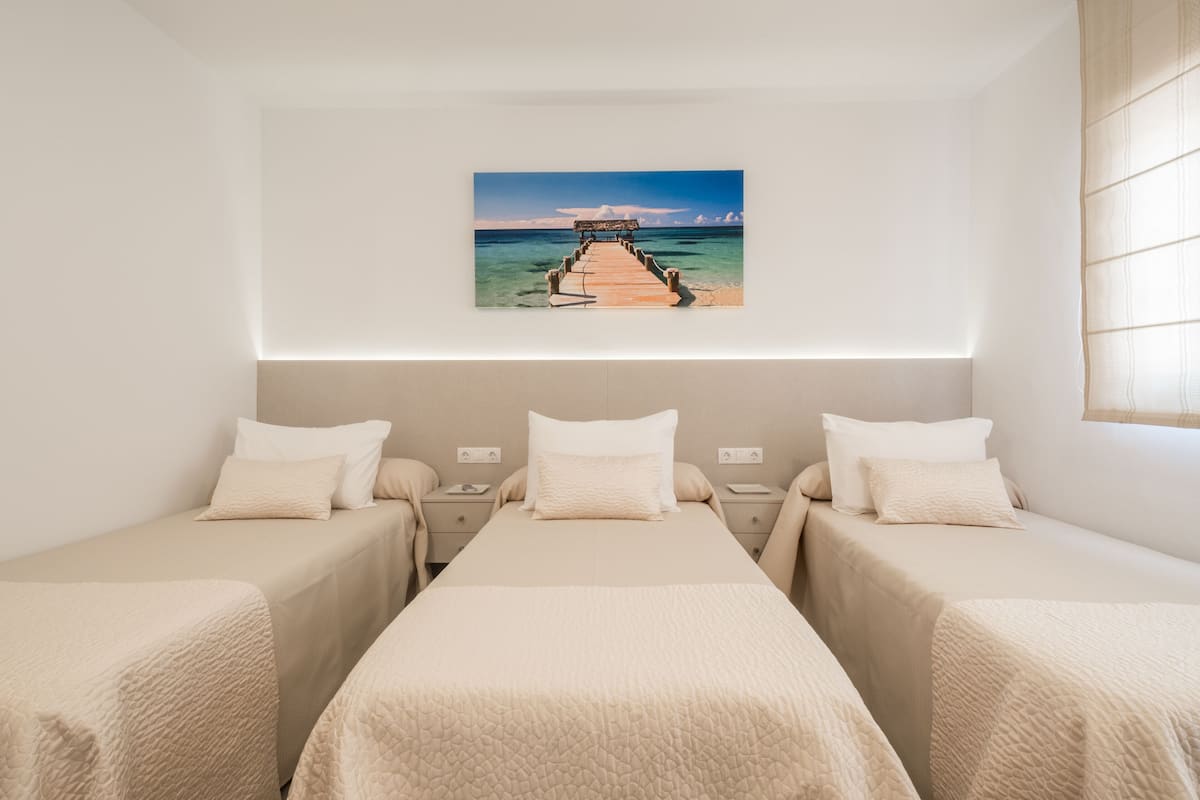 A hotel room with two single beds, a large window, and a painting of a pier on the wall.