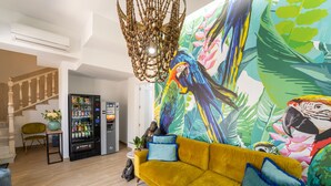 Una sala de estar con un sofá amarillo, un mural colorido, una máquina expendedora y una escalera.