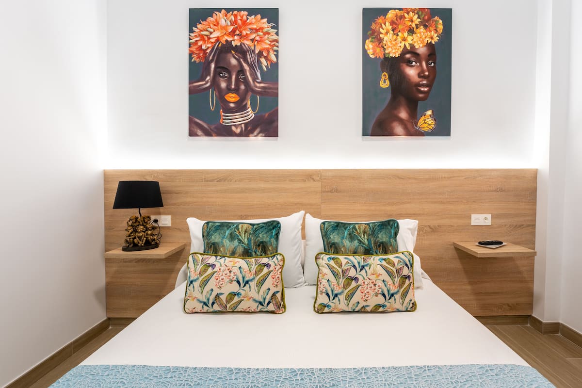 A neatly made bed with floral-patterned pillows, a wooden headboard, and two wall-mounted artworks depicting floral designs.