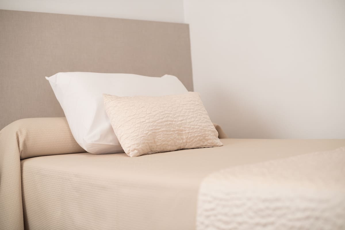 A bed with a beige headboard and two pillows, one white and one textured beige.