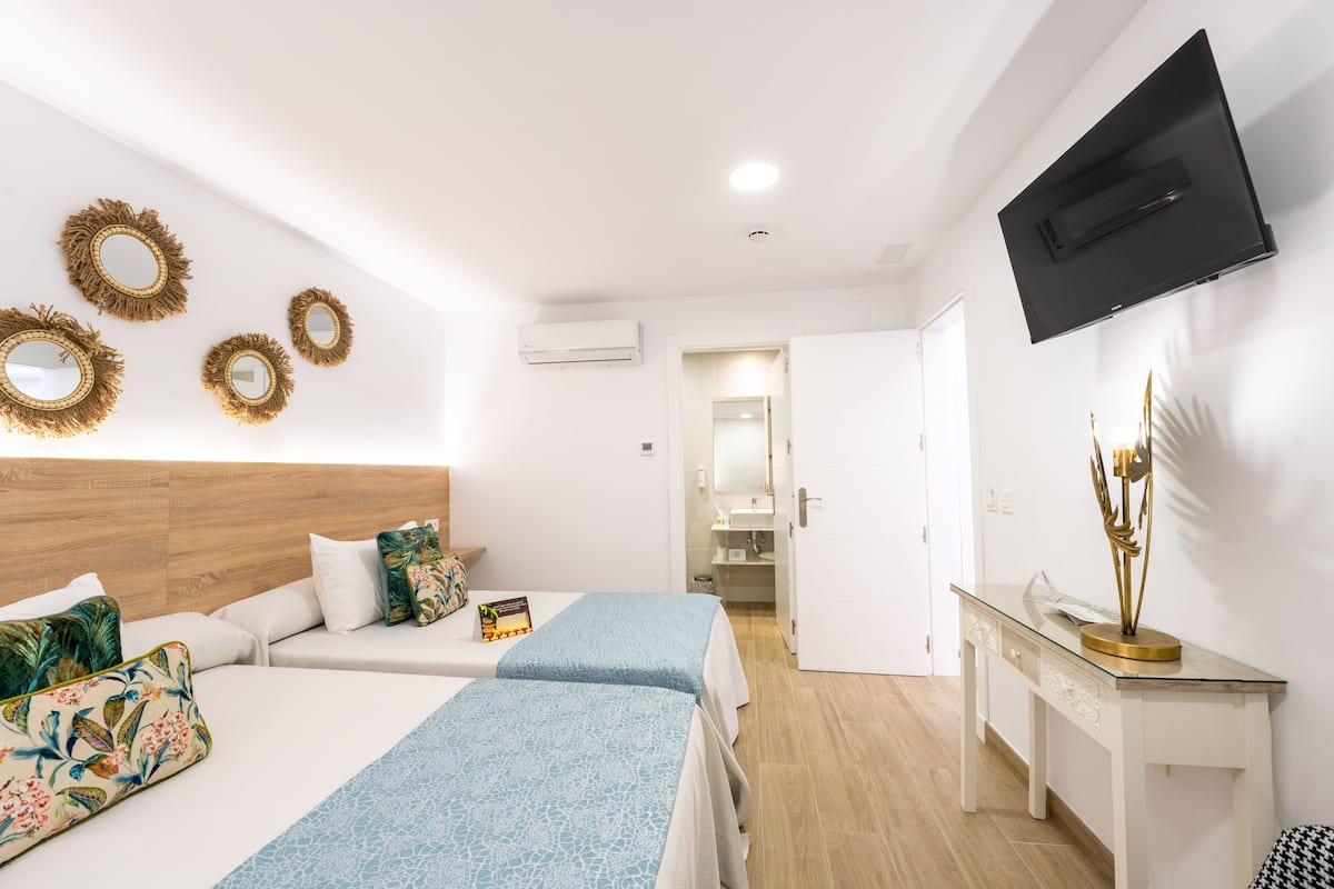 A hotel room with two beds, a wooden headboard, a glass console table, and a flat-screen TV mounted on the wall.