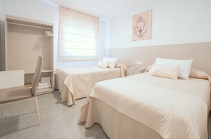 Una habitación de hotel con dos camas, un escritorio, una silla y una ventana con persianas.