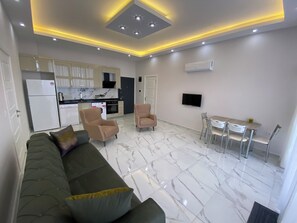 Ein modernes Wohnzimmer mit einer Couch, Sesseln, einem Esstisch und einer Küchenzeile mit Geräten.