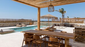 A wooden outdoor seating area with a pool, stone walls, and a clear view of the sea. - Cocopalm Villas Naxos (Naxos)