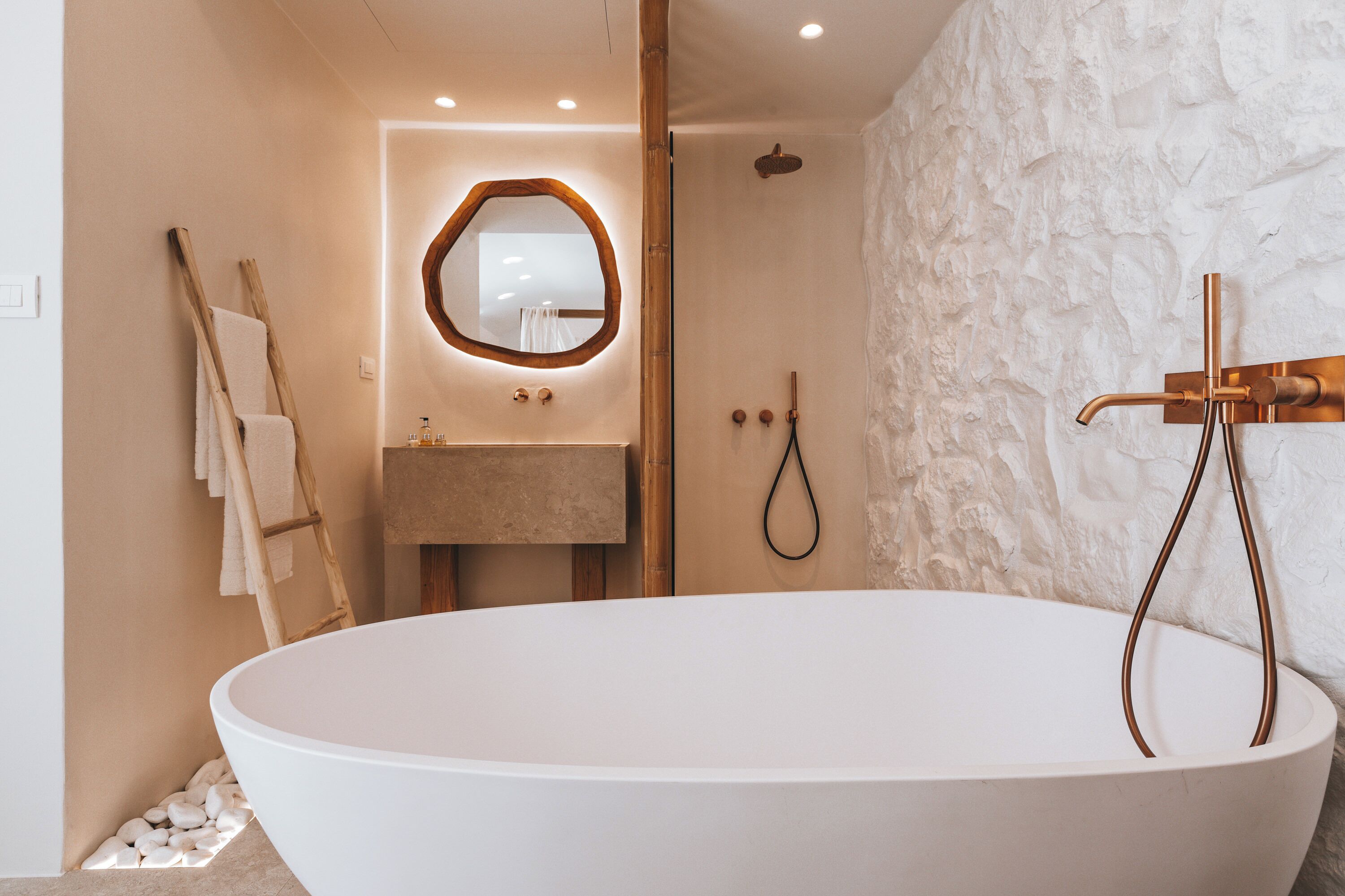 A modern bathroom with a freestanding bathtub, a wooden ladder, a stone wall, and a mirror with a wooden frame.