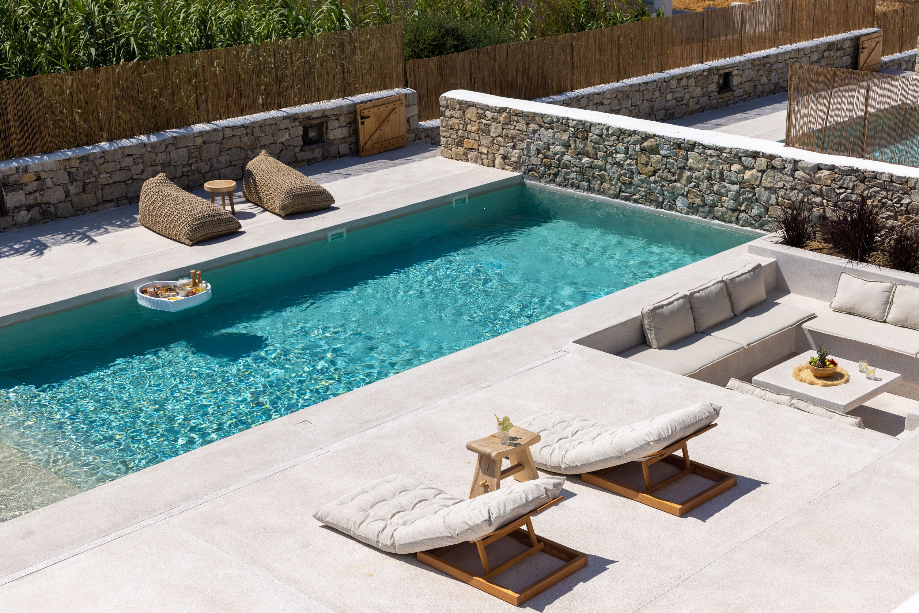 A pool area with lounge chairs, a small table, and a stone wall.