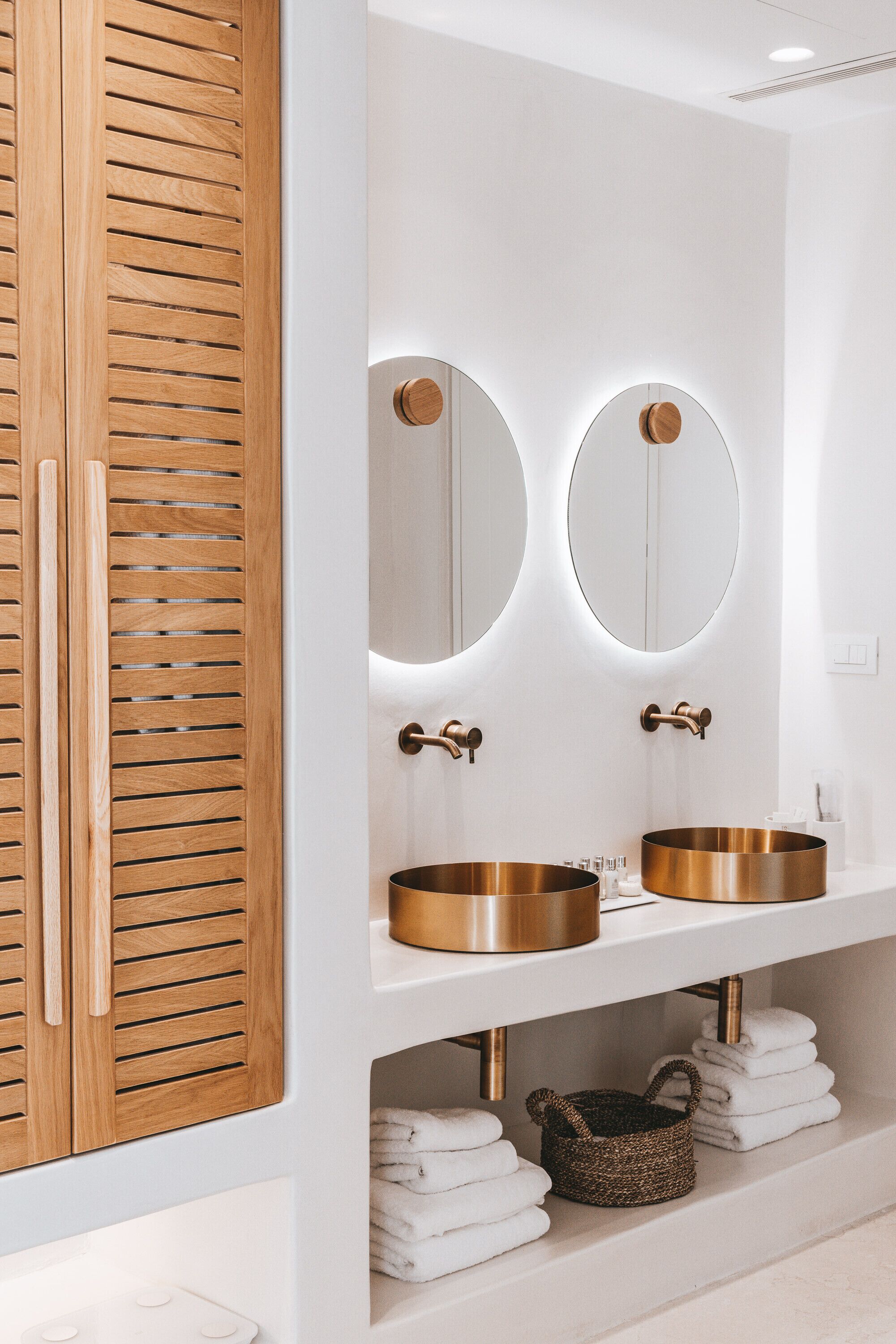 A modern bathroom with two sinks, wooden cabinets, and a mirror with circular frames.