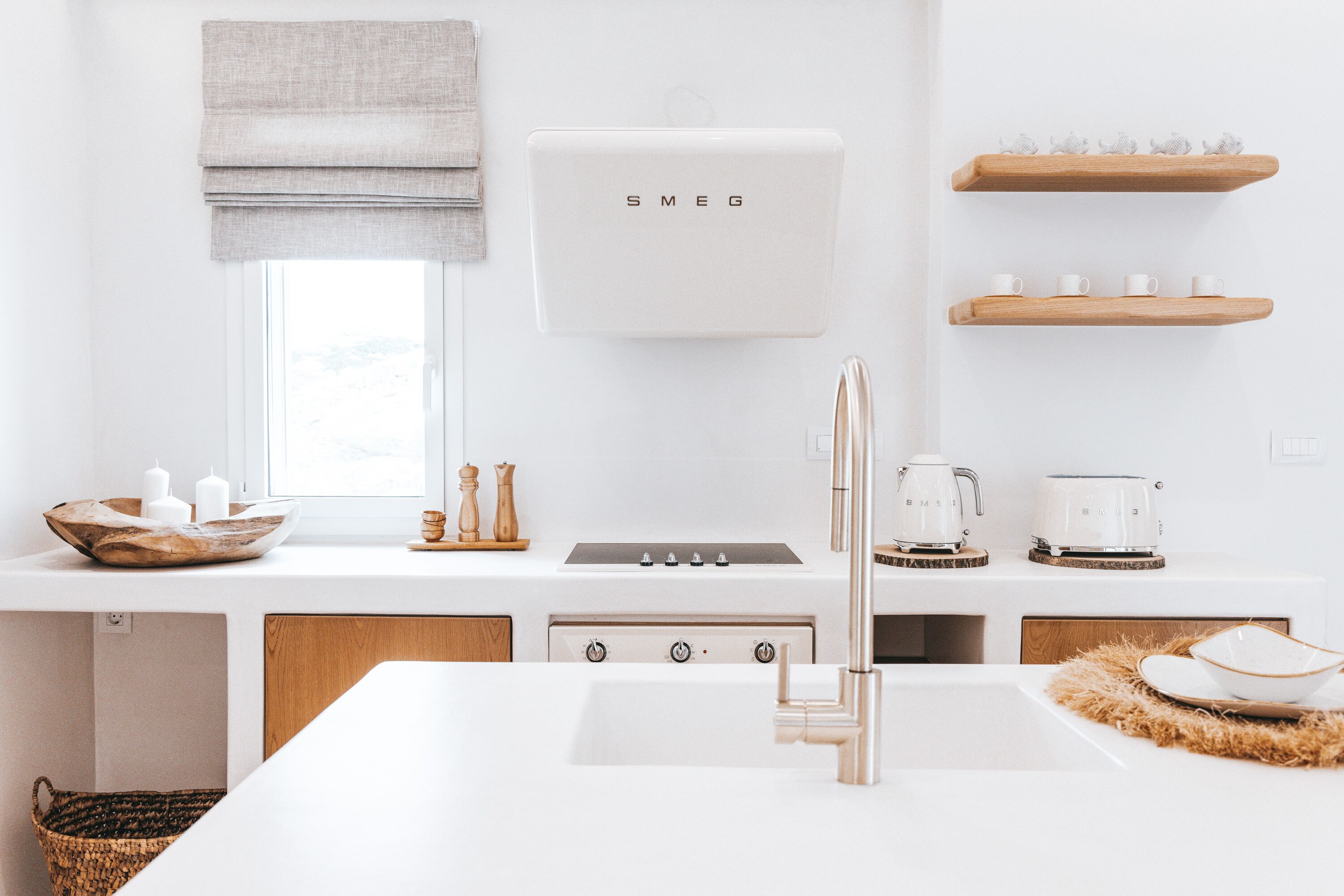 Una cocina moderna con encimera blanca, pileta de acero inoxidable, horno empotrado y cafetera.