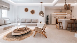 A modern living room with a sofa, a round coffee table, and a dining area with chairs and a kitchen in the background. - Cocopalm Villas Naxos (Naxos)