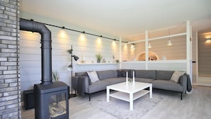 A modern living room with a black wood-burning stove, a gray sectional sofa, and a white coffee table. - Redewisch vacation apartment " Lee " (Boltenhagen/Redewisch)