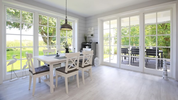 A bright dining area with a white table and chairs, large windows, and a hanging light fixture. - Redewisch vacation apartment " Lee " (Boltenhagen/Redewisch)