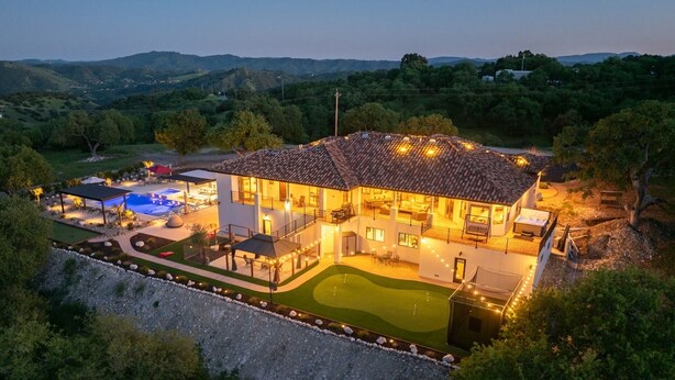 Una casa de dos pisos con piscina, mobiliario exterior y un jardín bien cuidado.