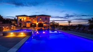 Una casa grande con piscina, mobiliario exterior y vistas al atardecer.