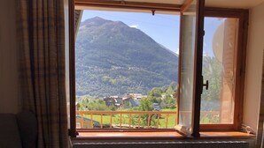A room with a view of a mountain, a sofa, two ottomans with red cushions, and a table with a remote control.