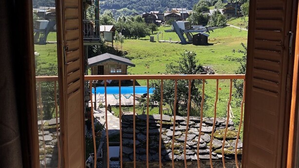 A wooden balcony with a view of a mountain, a swimming pool, and a stone wall.