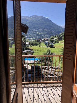 Een houten balkon met uitzicht op een berg, een zwembad en een stenen muur.