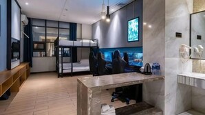 Moderni hotellihuone, jossa on kerrossänky, työpöytä tietokoneella, televisio sekä kylpyhuone, jossa on peili ja pesuallas.