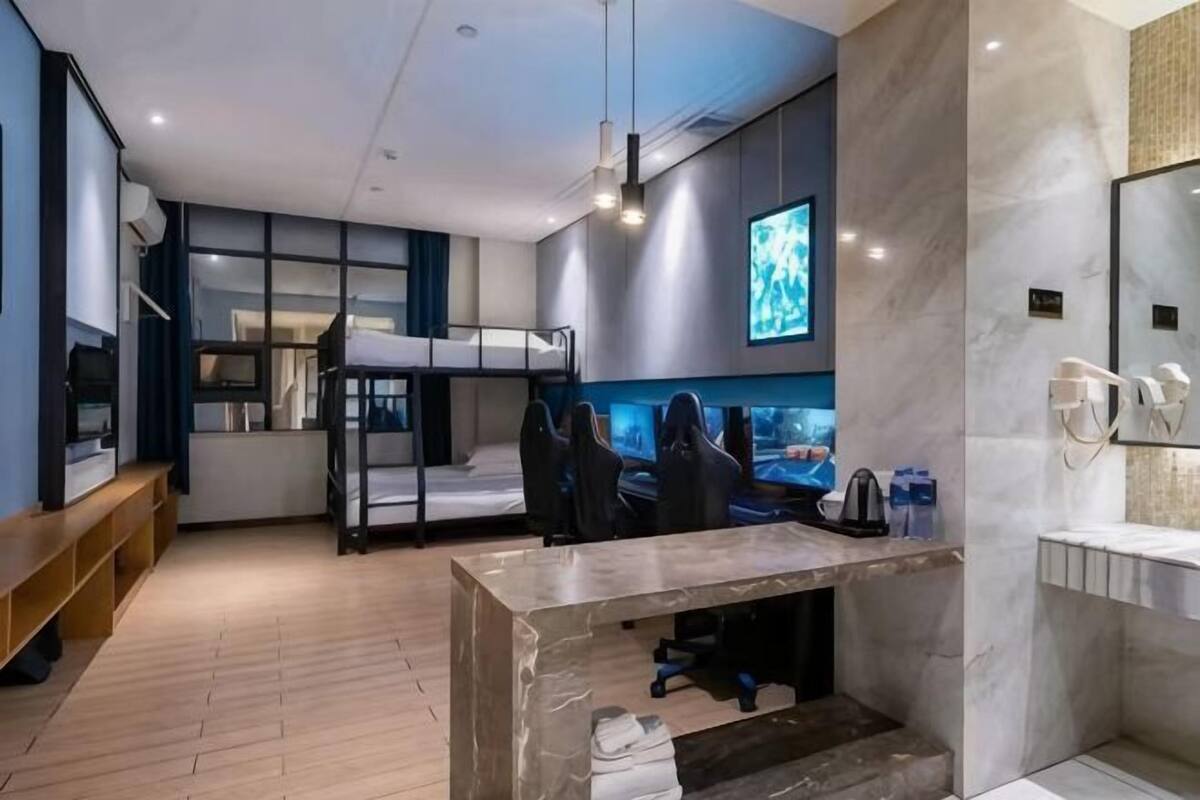 Une chambre d’hôtel moderne équipée d’un lit superposé, d’un bureau avec un ordinateur, d’une télévision et d’une salle de bain avec un miroir et un lavabo.