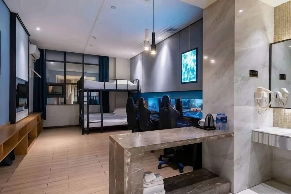 Ein modernes Hotelzimmer mit einem Etagenbett, einem Schreibtisch mit Computer, einem Fernseher und einem Badezimmer mit Spiegel und Waschbecken.