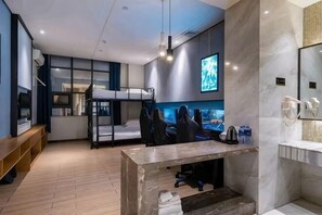 Ett modernt hotellrum med en våningssäng, ett skrivbord med en dator, en TV och ett badrum med spegel och handfat.