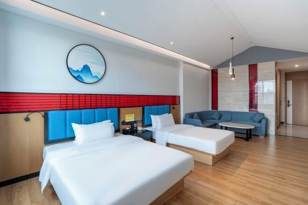 Una camera d'albergo con due letti, un divano, un tavolino e un'opera d'arte appesa al muro.