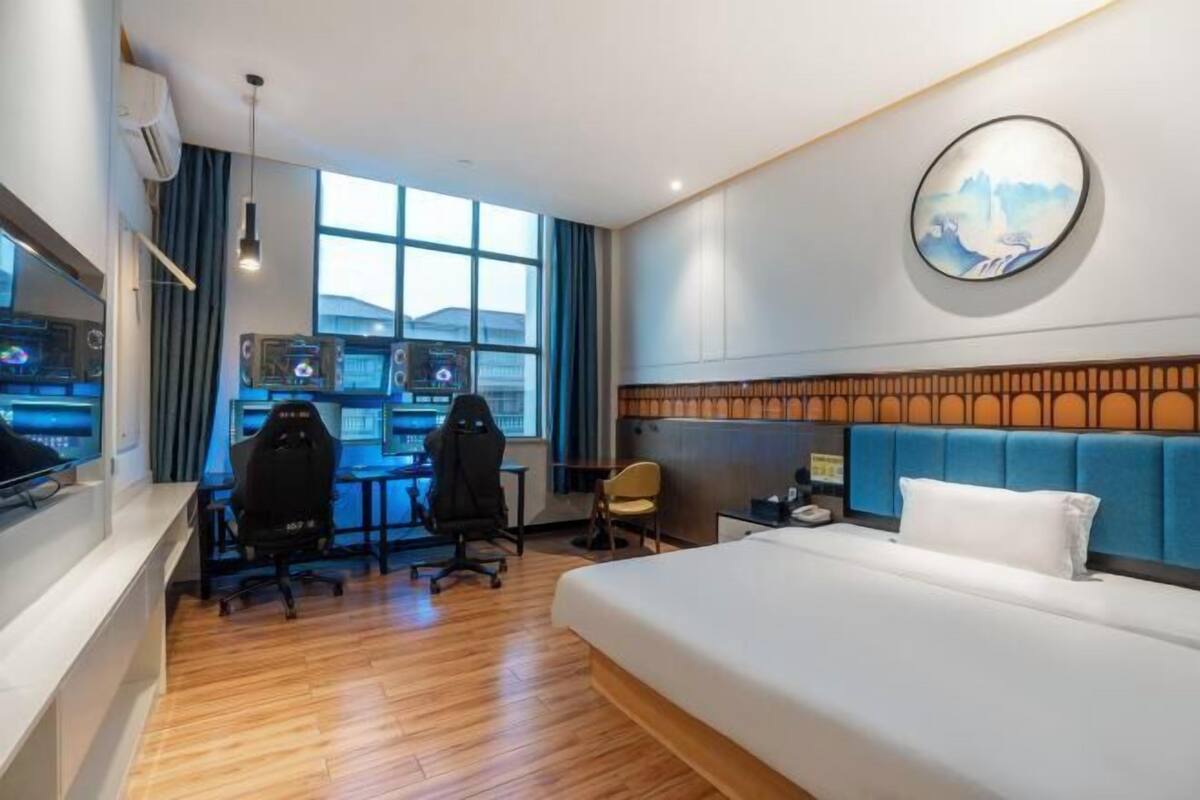 Une chambre d’hôtel avec un grand lit, un bureau doté de deux écrans, une chaise et un téléviseur fixé au mur.