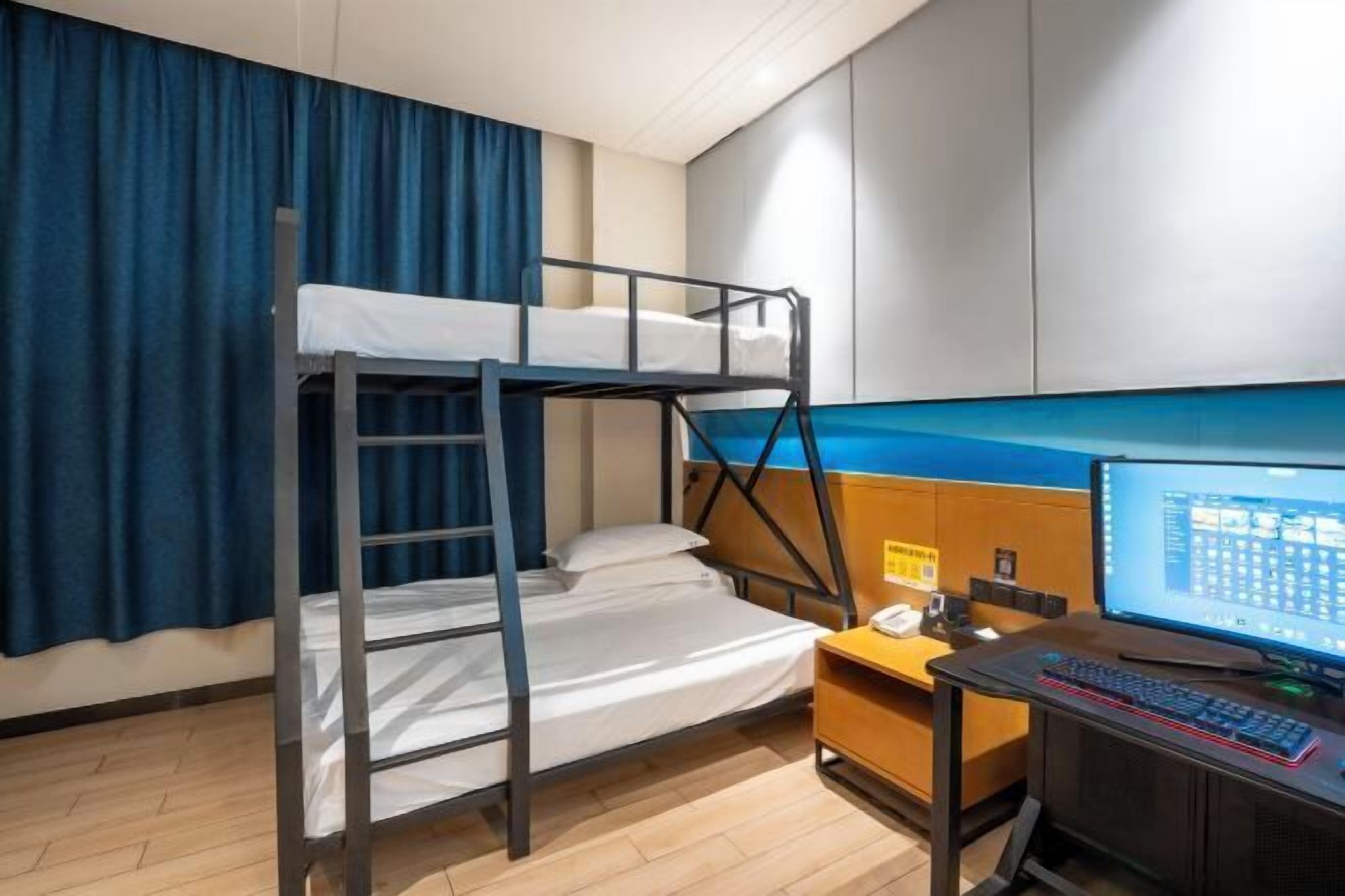 A bunk bed with a ladder, a desk with a computer, and a blue curtain.