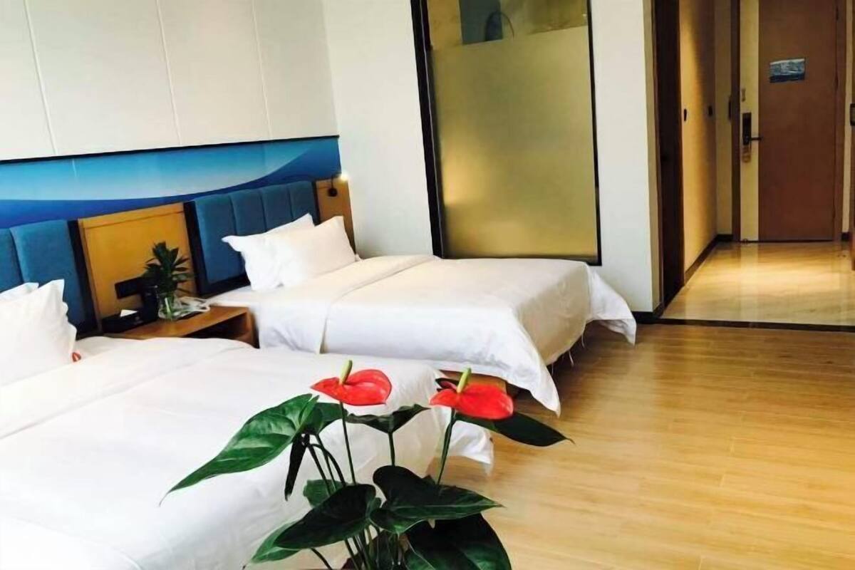 Une chambre d’hôtel avec deux lits, un plancher en bois et une plante aux fleurs rouges.