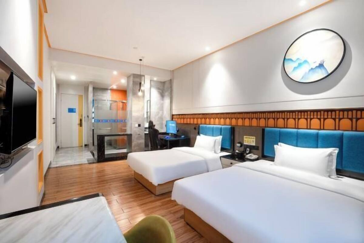 Une chambre d’hôtel avec deux lits, une télévision, un bureau et une salle de bain que l’on aperçoit à l’arrière-plan.