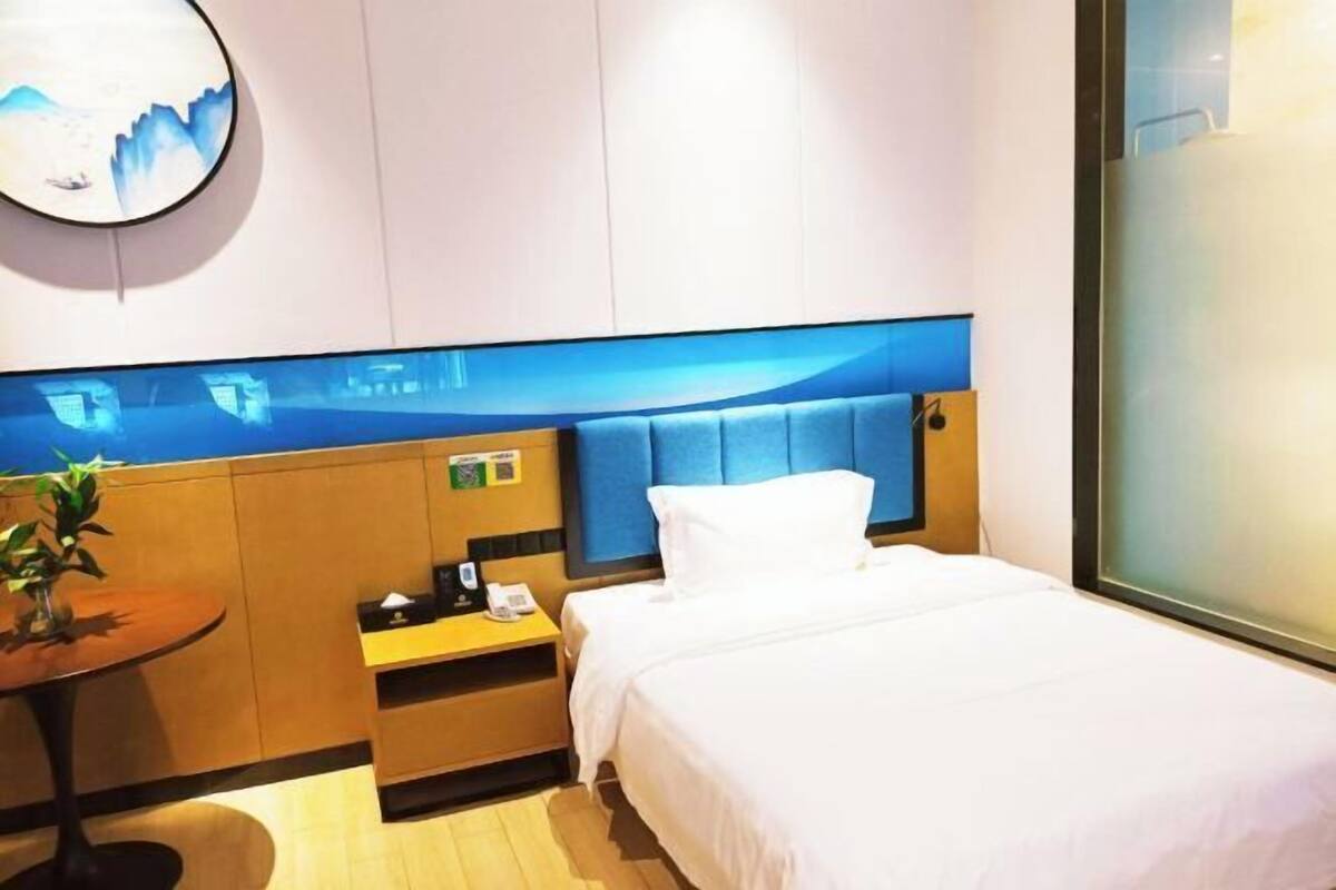 Une chambre d’hôtel comprenant un lit, un bureau, une chaise, une petite table avec une plante et une œuvre d’art accrochée au mur.