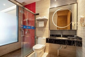 Un bany modern amb un espai de dutxa de vidre, un vàter, un lavabo amb taulell de marbre i un gran mirall amb llum circular.