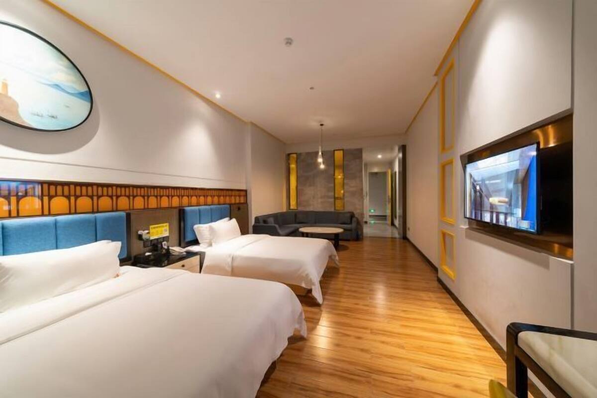 Une chambre d’hôtel avec deux lits, un canapé, une télévision et un plancher en bois.
