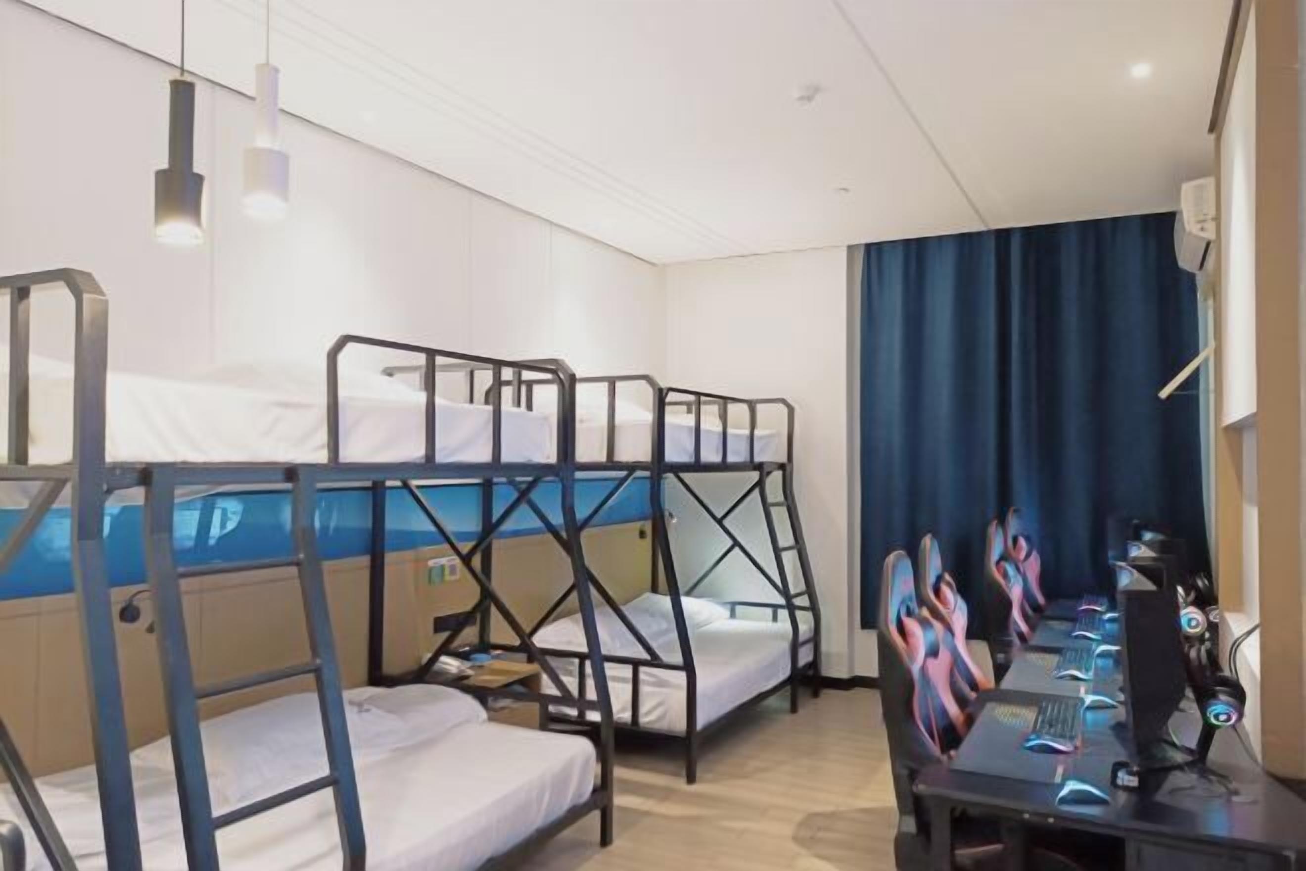 A bunk bed room with a desk and chairs, a computer, and a curtain.