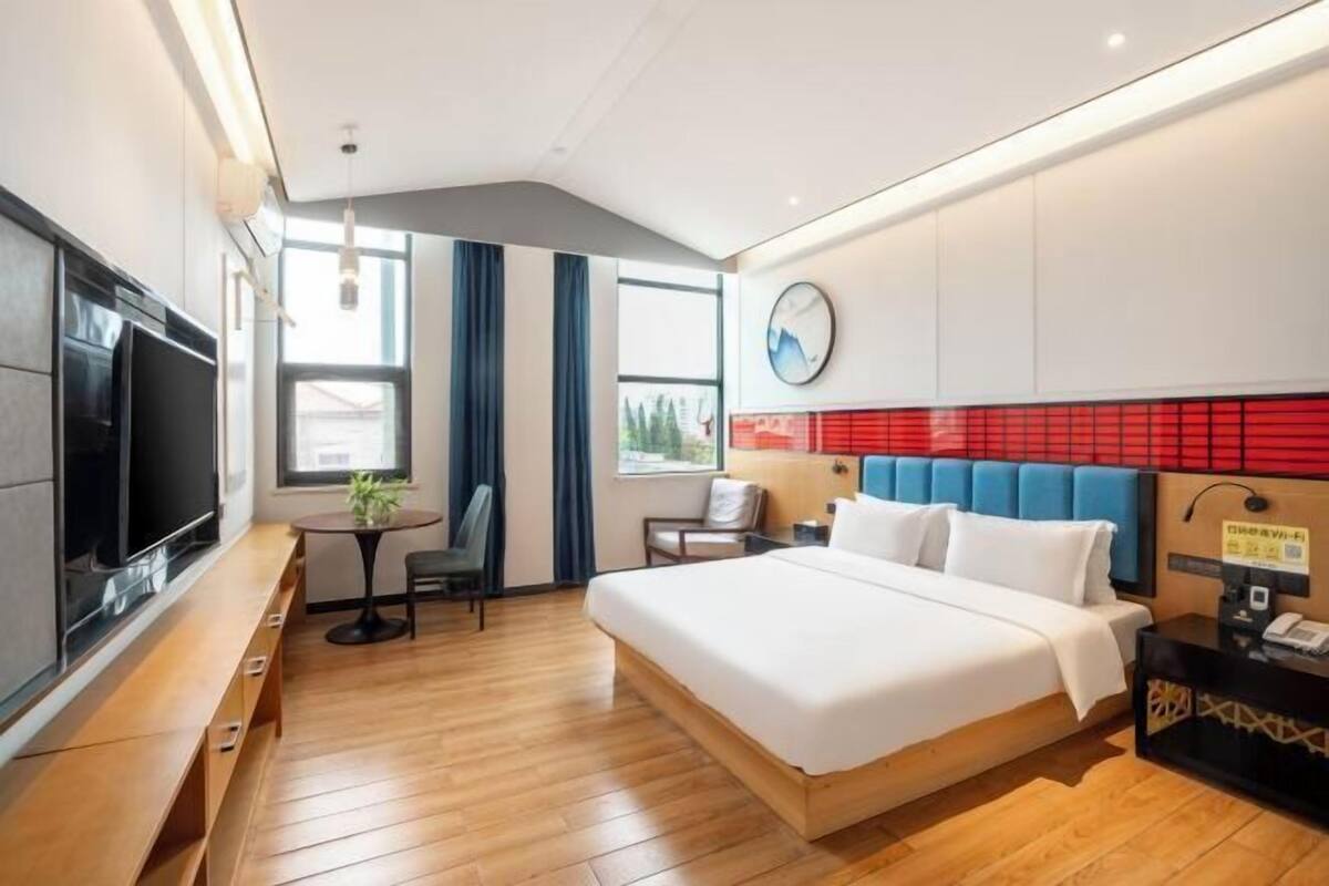 Une chambre d’hôtel avec un lit, un bureau, une télévision, une horloge et une fenêtre.