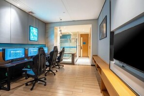 Un moderno spazio ufficio con monitor multipli, sedie ergonomiche, un'ampia TV a schermo piatto e un'area conferenze con pareti in vetro.