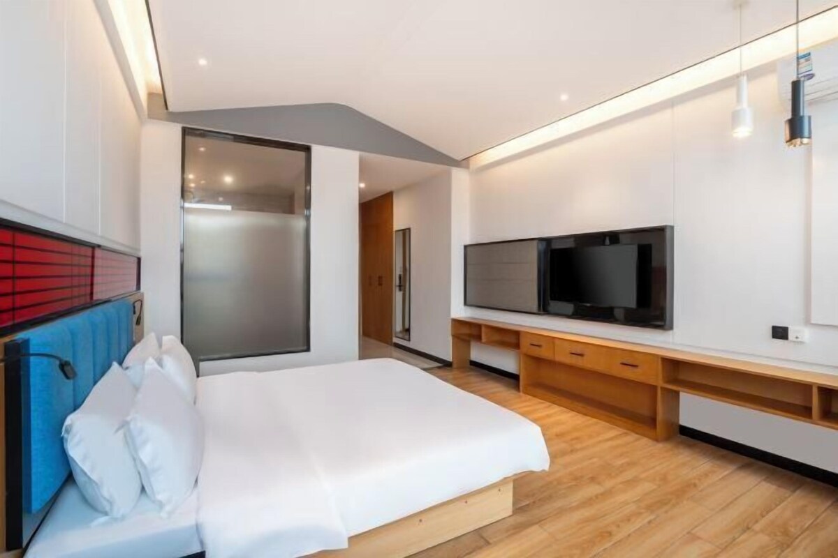 Camera d'albergo moderna con un letto grande, una TV a schermo piatto, pavimento in legno e una porta scorrevole in vetro che dà accesso al bagno.