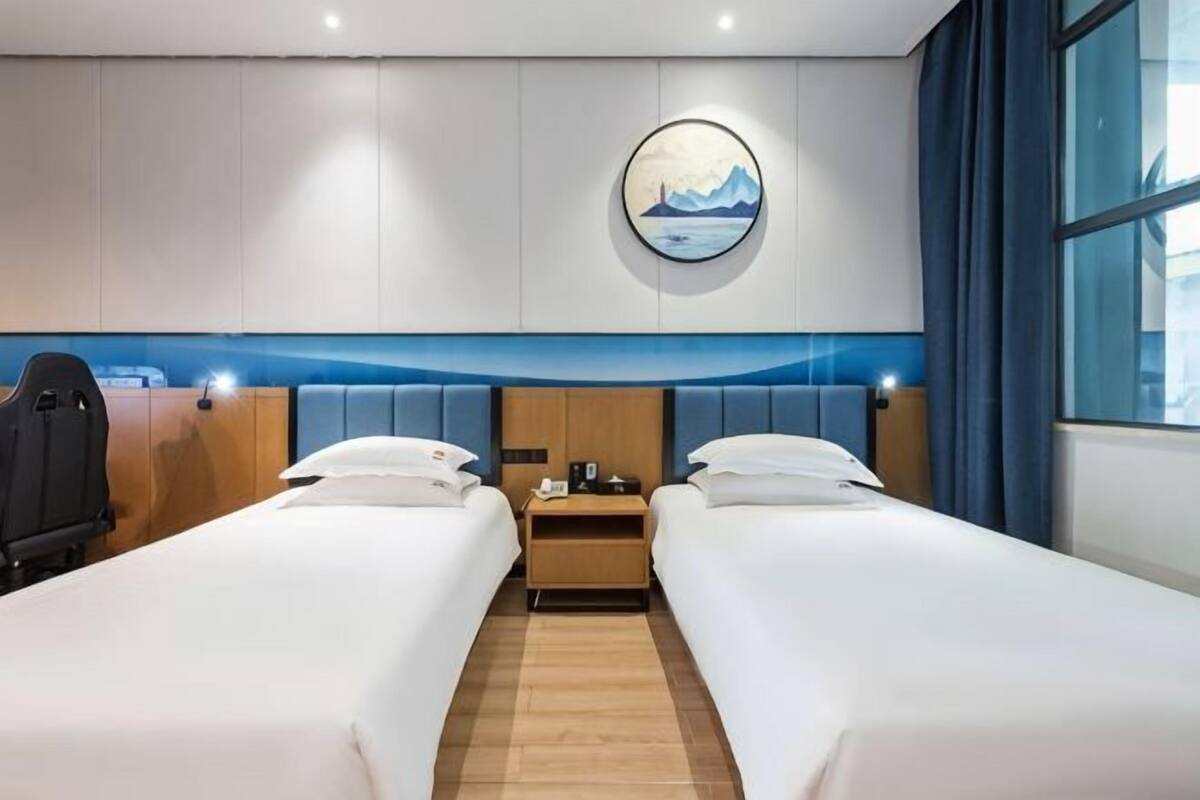Une chambre d’hôtel avec deux lits, une table de chevet, un bureau, une chaise et une grande fenêtre.
