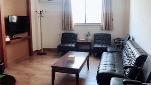 Una sala de estar con un sofá, dos sillones, una mesa de centro, un televisor y un perchero.