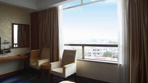 Habitación de hotel con un ventanal grande, dos sillones, una mesita y un escritorio con lámpara.
