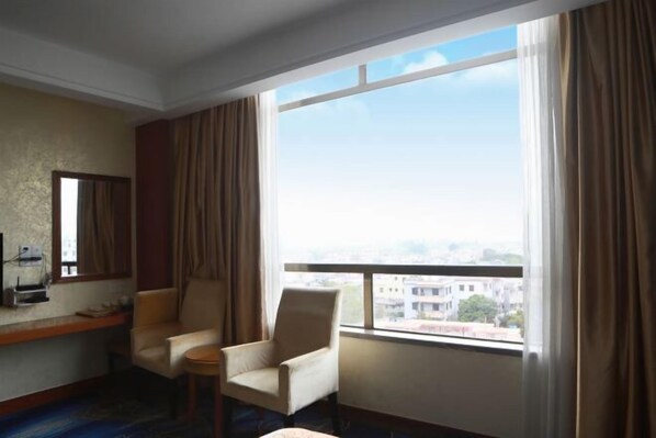 Habitación de hotel con dos sillones, una mesita, una ventana con cortinas y vistas a edificios.