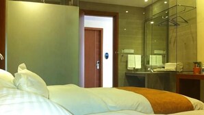Habitación de hotel con cama, baño con cabina de ducha de vidrio y puerta que da a otra habitación.
