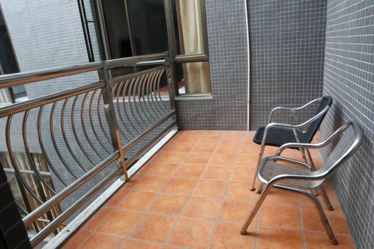 Un balcón con barandilla de metal, piso de baldosas y dos sillas metálicas.