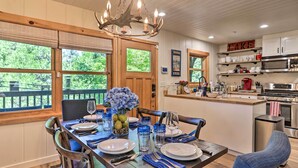 A dining area with a wooden table set for four, a chandelier, and a view of the outdoors. - Steps to Lake: Cabin w/ Deck in Lake Arrowhead (Lake Arrowhead)