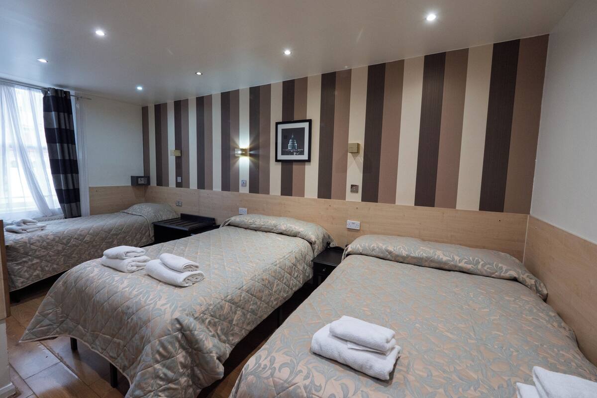 A hotel room with two beds, each with a duvet and a pillow. There is a nightstand between the beds, and a framed picture on the wall.