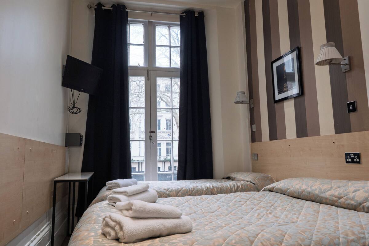 A hotel room with two beds, a TV, a picture on the wall, and a window with curtains.