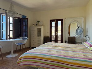 A bedroom with a bed, a desk, a chair, a wardrobe, and a window with shutters.